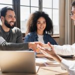 A couple shaking hands with a professional at a meeting table.