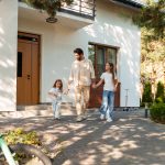 A father walking toward the entryway of a house alongside his two daughters.