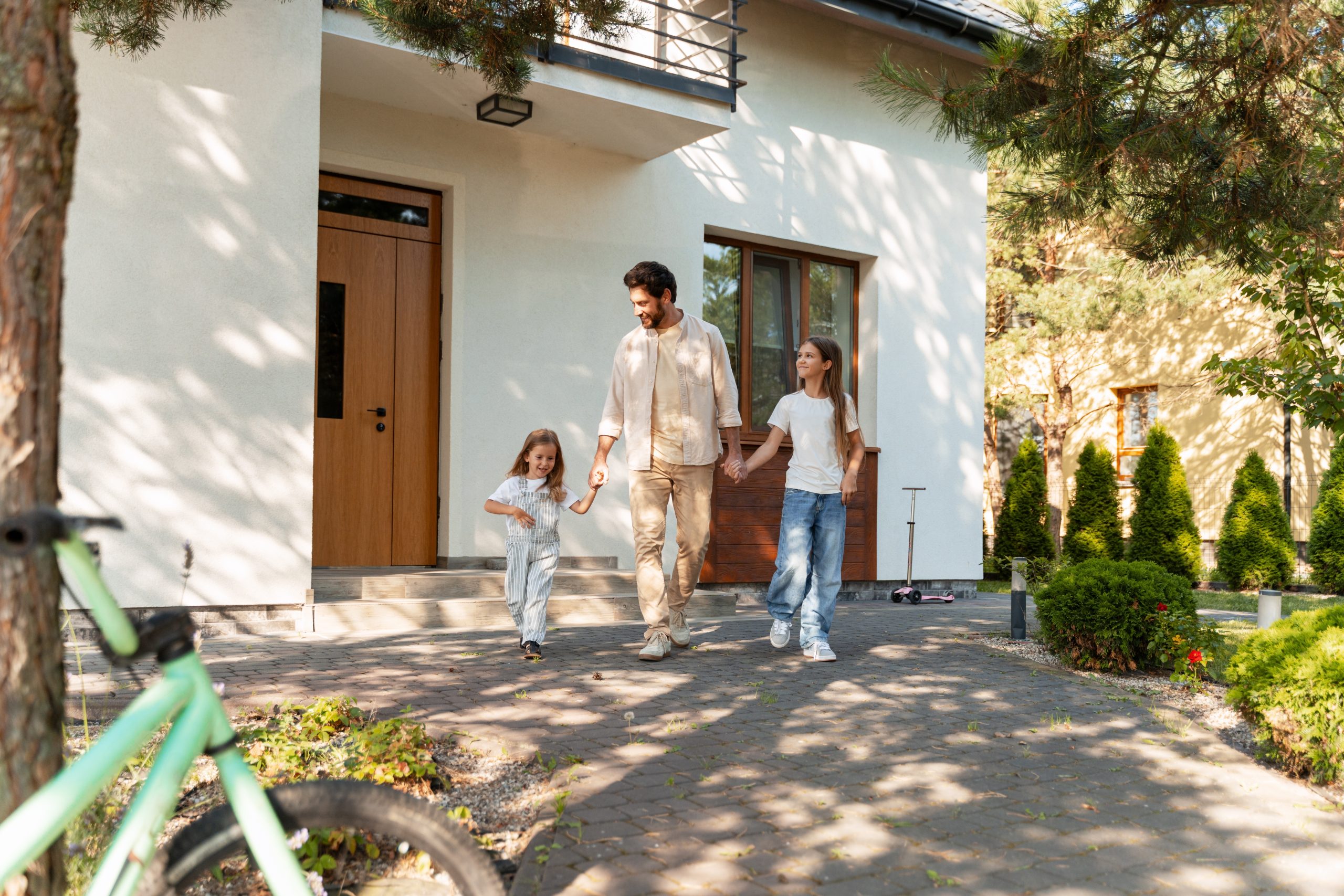 A father walking toward the entryway of a house alongside his two daughters.