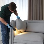 A pest control technician inspecting a grey sofa with a flashlight.